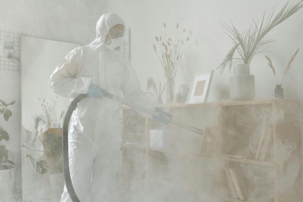 Individual in protective suit and mask sanitizing a room with smoke fumigation.